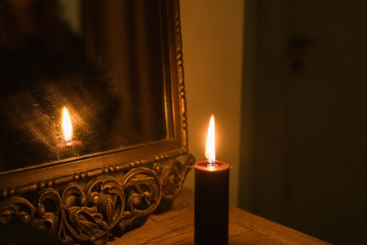 Vela acesa diante de um espelho dourado, refletindo a chama