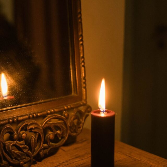 Vela acesa diante de um espelho dourado, refletindo a chama