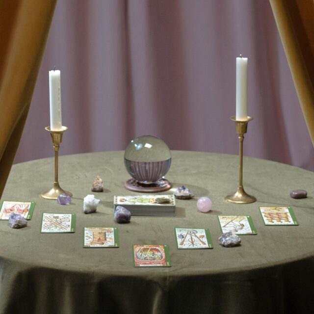 Mesa redonda com cartas, velas e bola de cristal entre cortinas douradas