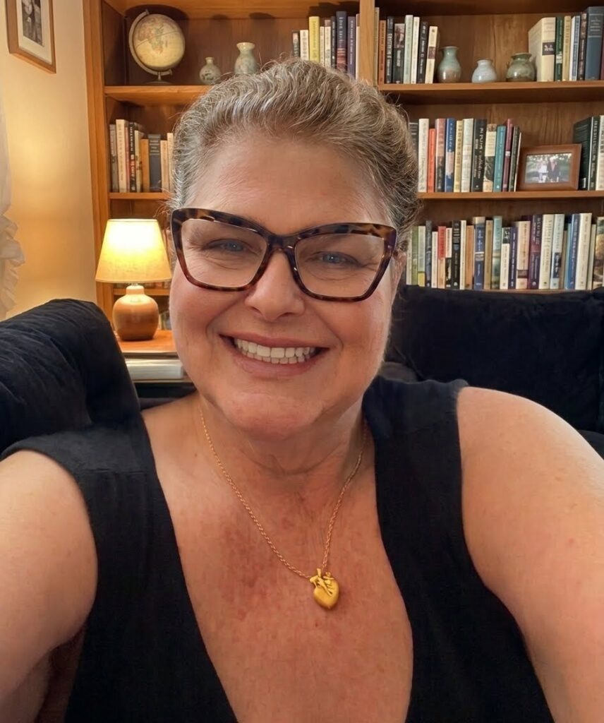 Barbara Mariah sorrindo em ambiente acolhedor com biblioteca ao fundo